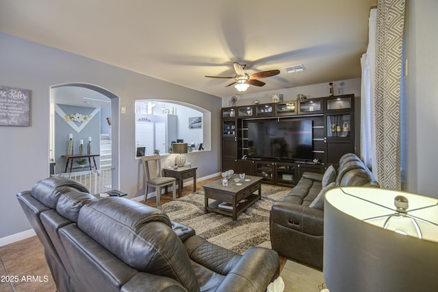 living room featuring tile patterned floors, baseboards, visible vents, arched walkways, and ceiling fan