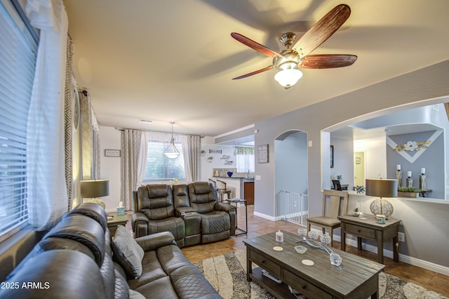 living room with visible vents, baseboards, ceiling fan, arched walkways, and light tile patterned floors