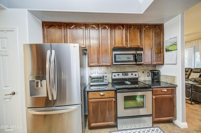 kitchen featuring dark stone countertops, light tile patterned floors, a toaster, stainless steel appliances, and decorative backsplash