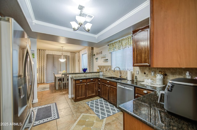 kitchen with a peninsula, ornamental molding, stainless steel appliances, a raised ceiling, and a sink