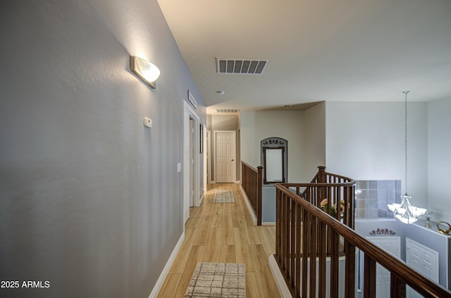 corridor featuring an upstairs landing, a chandelier, light wood-type flooring, baseboards, and visible vents