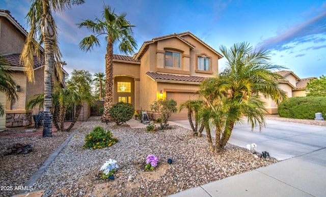 mediterranean / spanish-style home with stucco siding, an attached garage, a tiled roof, and concrete driveway