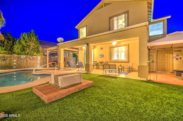 back of house at night featuring stucco siding, fence, a patio, and a fenced in pool