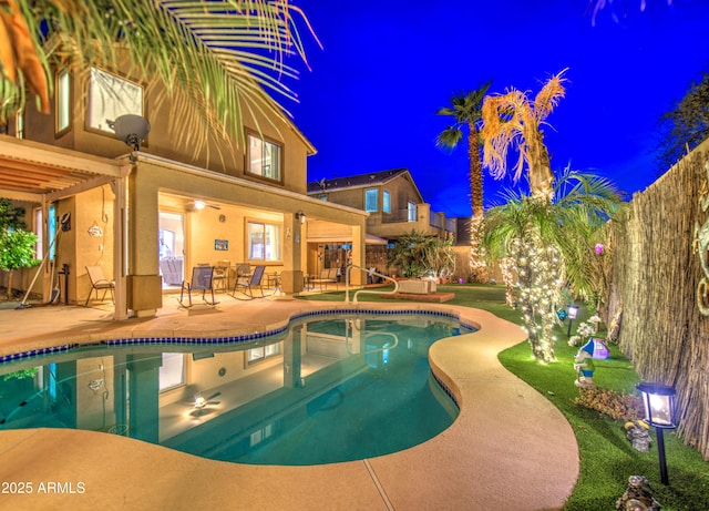 pool at night with a fenced backyard, an outdoor pool, and a patio area