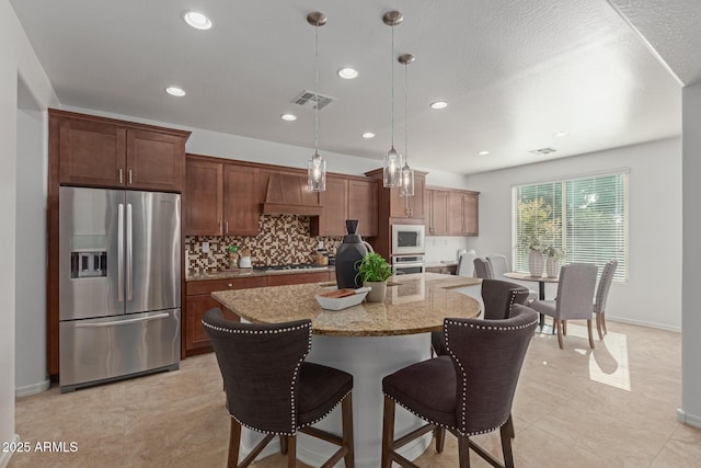 kitchen featuring light stone counters, decorative light fixtures, stainless steel appliances, a kitchen island with sink, and decorative backsplash