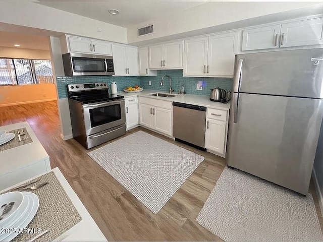 kitchen with appliances with stainless steel finishes, light hardwood / wood-style floors, white cabinets, and sink