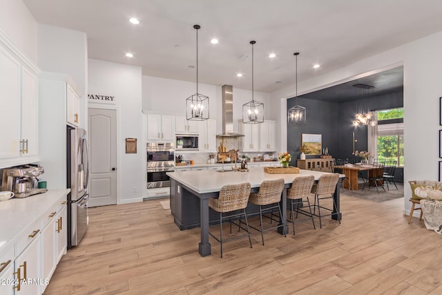 kitchen with pendant lighting, appliances with stainless steel finishes, wall chimney exhaust hood, and light wood-type flooring