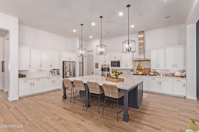 kitchen featuring appliances with stainless steel finishes, a kitchen breakfast bar, a kitchen island with sink, white cabinets, and wall chimney range hood