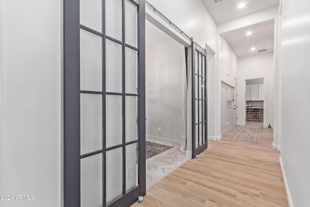 corridor featuring a high ceiling, a barn door, and light hardwood / wood-style flooring