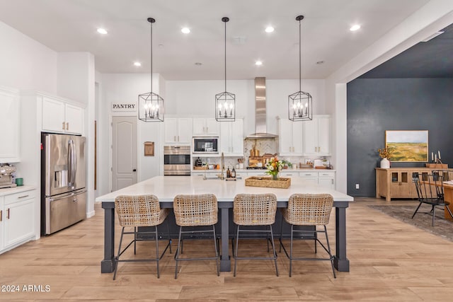 kitchen featuring stainless steel appliances, a large island with sink, a breakfast bar area, and wall chimney range hood