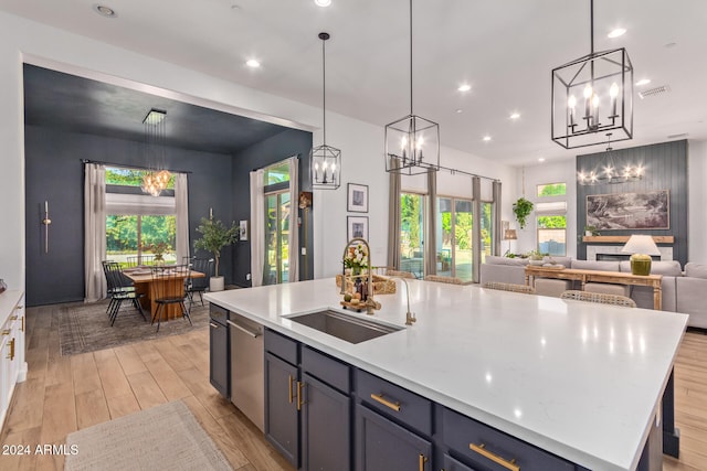 kitchen featuring a center island with sink, sink, light wood-type flooring, and decorative light fixtures