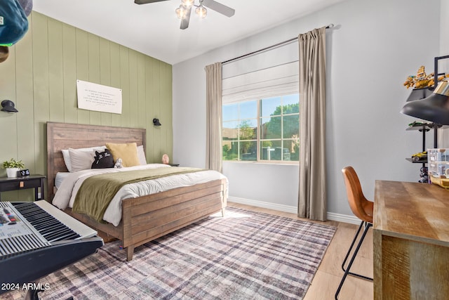 bedroom with light hardwood / wood-style floors, ceiling fan, and wooden walls