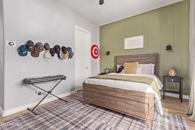 bedroom with ceiling fan, wood-type flooring, and wooden walls