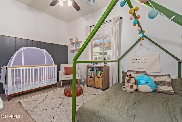 carpeted bedroom with a nursery area, wood walls, and ceiling fan