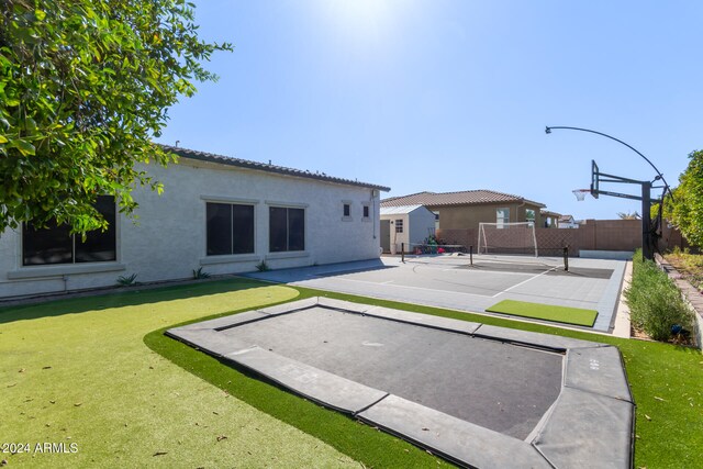 rear view of house featuring tennis court, a lawn, and basketball hoop