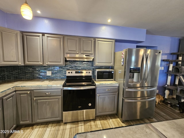 kitchen featuring stainless steel appliances, light wood-type flooring, decorative backsplash, and tile counters