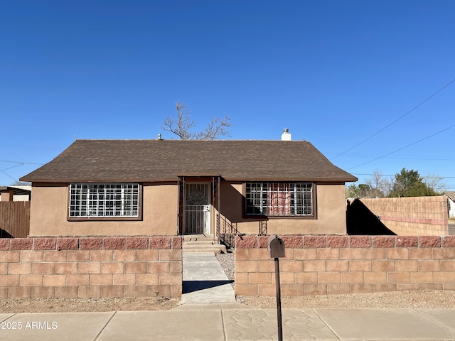 view of front of house with a fenced front yard, roof with shingles, and stucco siding