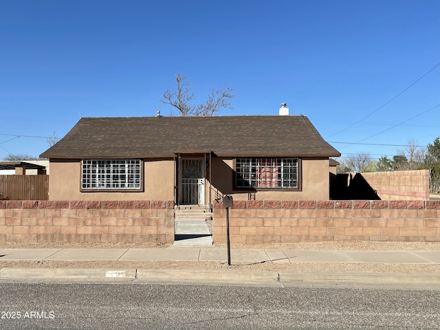 view of front of home featuring roof with shingles, a fenced front yard, a chimney, and stucco siding