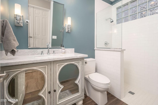 bathroom featuring hardwood / wood-style flooring, toilet, vanity, and a tile shower