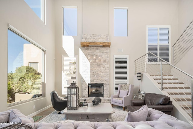 living room with a towering ceiling, plenty of natural light, wood-type flooring, and a stone fireplace