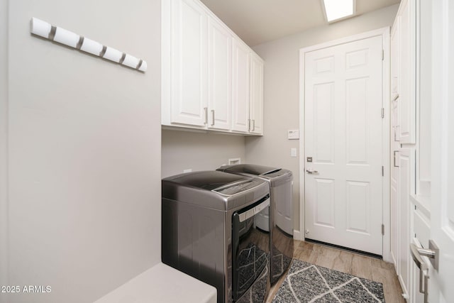 laundry area with light wood-type flooring, washer and dryer, and cabinets