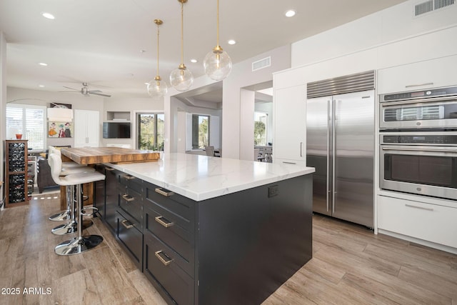 kitchen featuring decorative light fixtures, ceiling fan, white cabinetry, appliances with stainless steel finishes, and light stone countertops