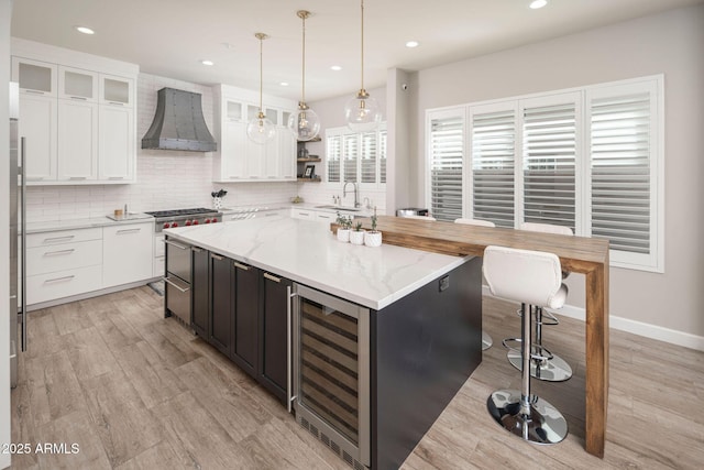 kitchen with white cabinetry, wall chimney range hood, a kitchen island, pendant lighting, and light stone counters