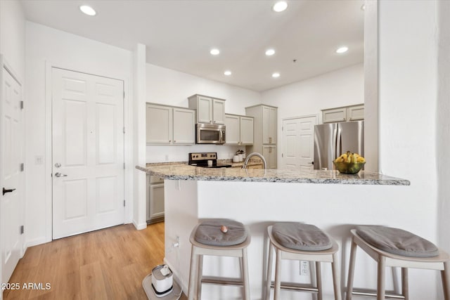 kitchen with a peninsula, light wood-style floors, a kitchen breakfast bar, gray cabinets, and stainless steel appliances