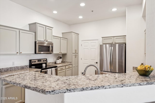 kitchen with gray cabinets, appliances with stainless steel finishes, light stone counters, a peninsula, and recessed lighting