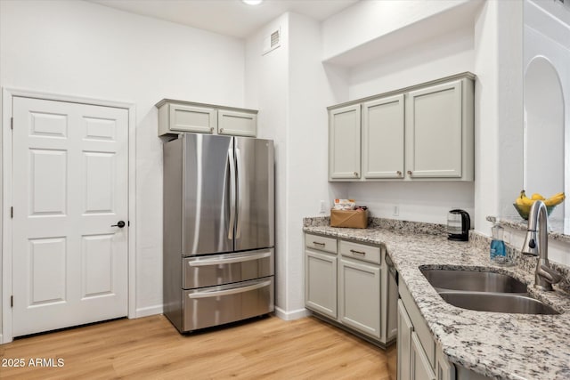 kitchen with gray cabinets, light stone countertops, light wood-type flooring, a sink, and stainless steel appliances