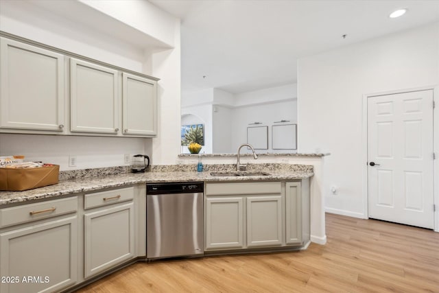 kitchen with stainless steel dishwasher, a peninsula, light stone counters, a sink, and light wood finished floors