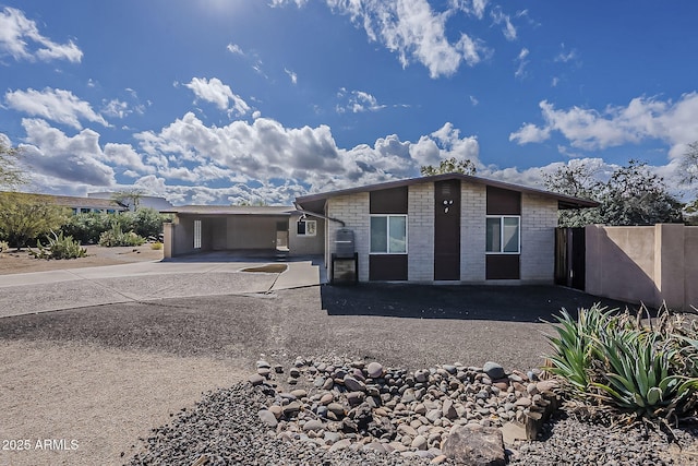 view of front facade with an attached carport, concrete driveway, brick siding, and fence