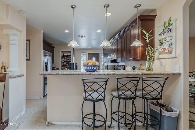 kitchen with under cabinet range hood, a breakfast bar area, a peninsula, stainless steel refrigerator with ice dispenser, and light tile patterned flooring