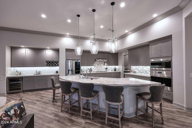 kitchen featuring stainless steel appliances, tasteful backsplash, wine cooler, a large island with sink, and decorative light fixtures