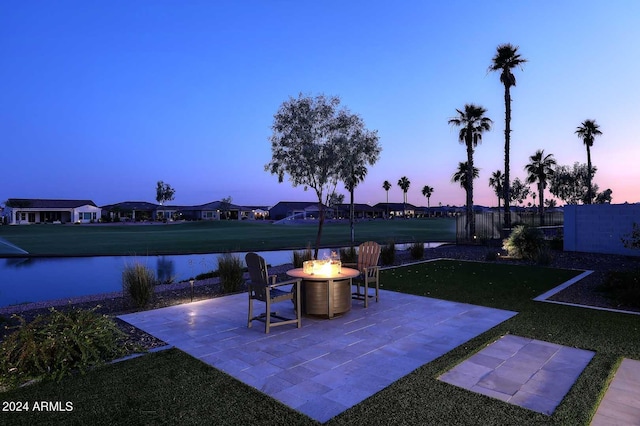 patio terrace at dusk with a yard, a water view, and an outdoor fire pit