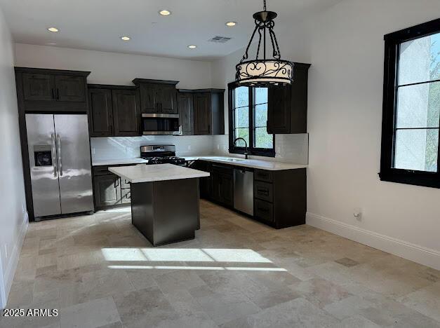 kitchen with appliances with stainless steel finishes, backsplash, sink, pendant lighting, and a center island