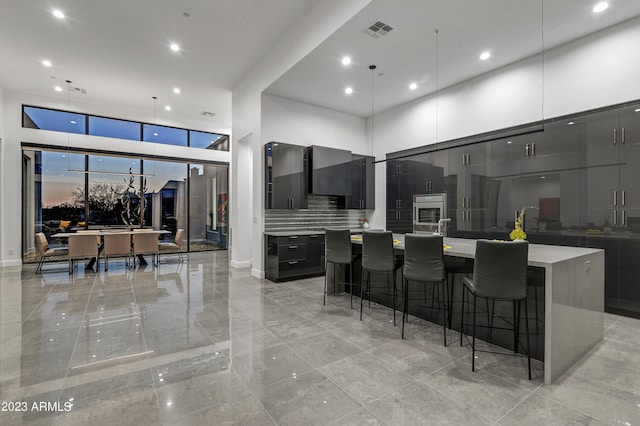 kitchen featuring a large island with sink, stainless steel oven, hanging light fixtures, decorative backsplash, and a breakfast bar area