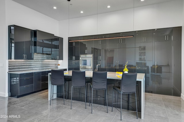 kitchen with a kitchen island with sink, oven, hanging light fixtures, a kitchen bar, and tasteful backsplash