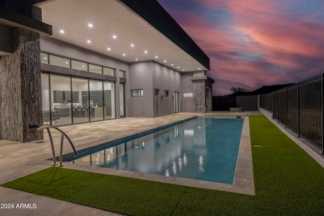 pool at dusk featuring a patio and a lawn