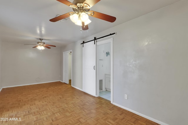 spare room with ceiling fan, a barn door, and baseboards