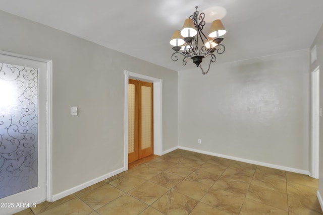 unfurnished room featuring baseboards and an inviting chandelier