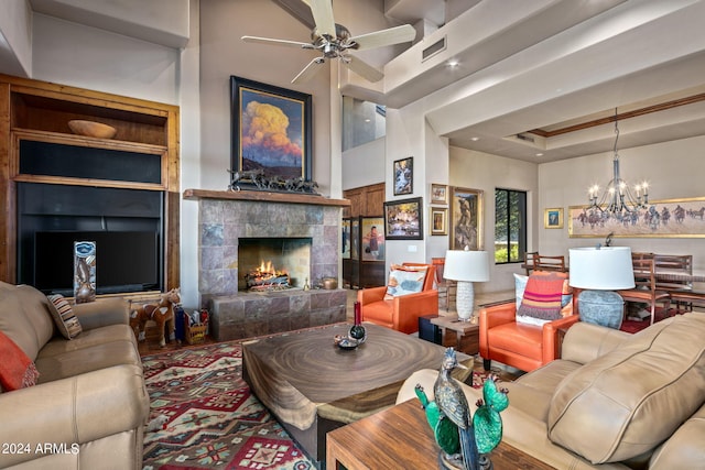 living room with ceiling fan with notable chandelier, a towering ceiling, a raised ceiling, and a tile fireplace