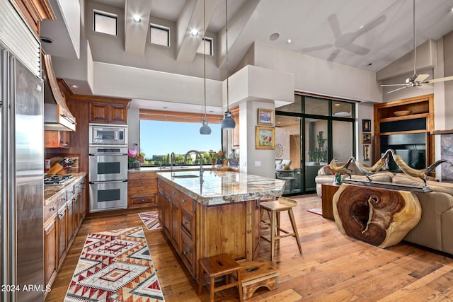 kitchen with light stone counters, light wood-type flooring, hanging light fixtures, and high vaulted ceiling