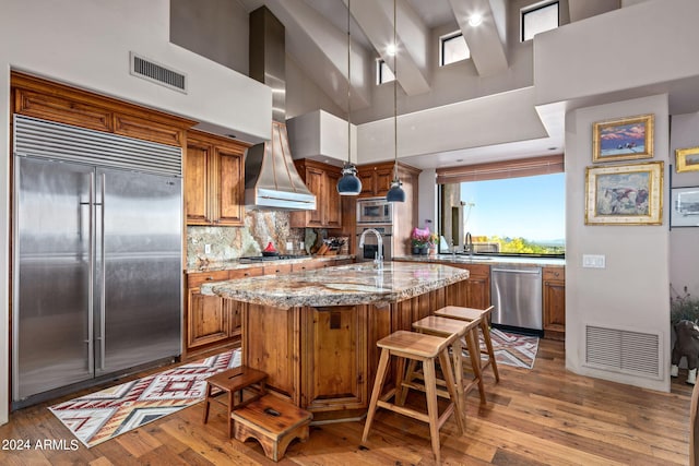 kitchen featuring a high ceiling, a kitchen breakfast bar, built in appliances, a kitchen island with sink, and light wood-type flooring