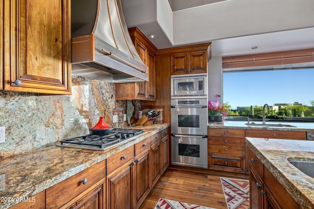 kitchen featuring custom exhaust hood, light stone counters, sink, and appliances with stainless steel finishes