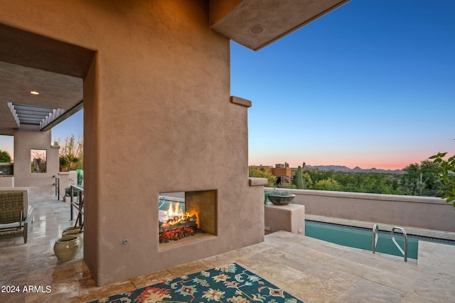 pool at dusk with a patio area and a multi sided fireplace