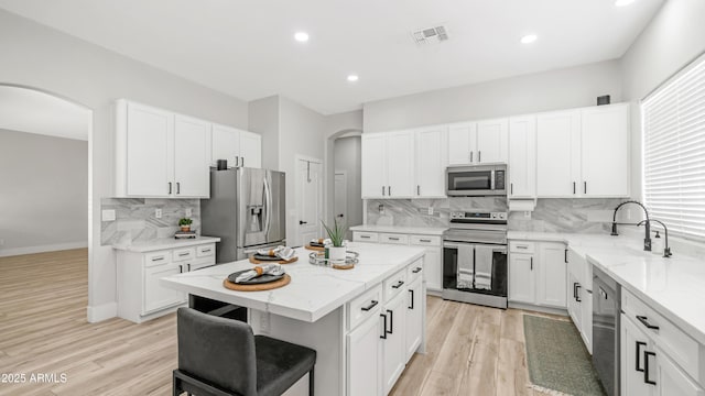 3103 S Benton, Mesa, AZ 85212 - kitchen with stainless steel appliances, arched walkways, a kitchen island, decorative backsplash, and light stone counters