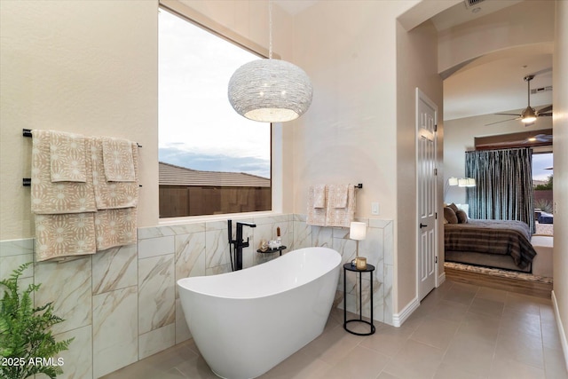 bathroom with ceiling fan, tile walls, a tub to relax in, and tile patterned floors