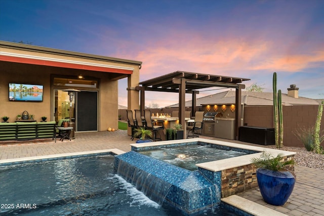 pool at dusk featuring an in ground hot tub, an outdoor kitchen, exterior bar, a patio, and pool water feature