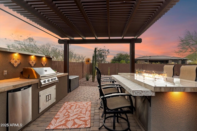 patio terrace at dusk featuring an outdoor bar, a grill, and area for grilling